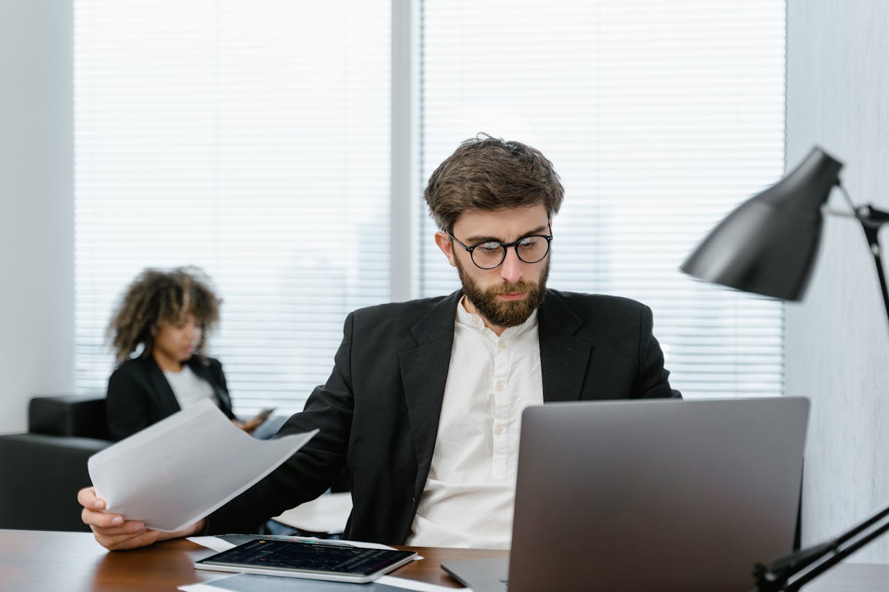 Two business professionals analyzing data on a laptop in a modern office setting, focusing on strategy.