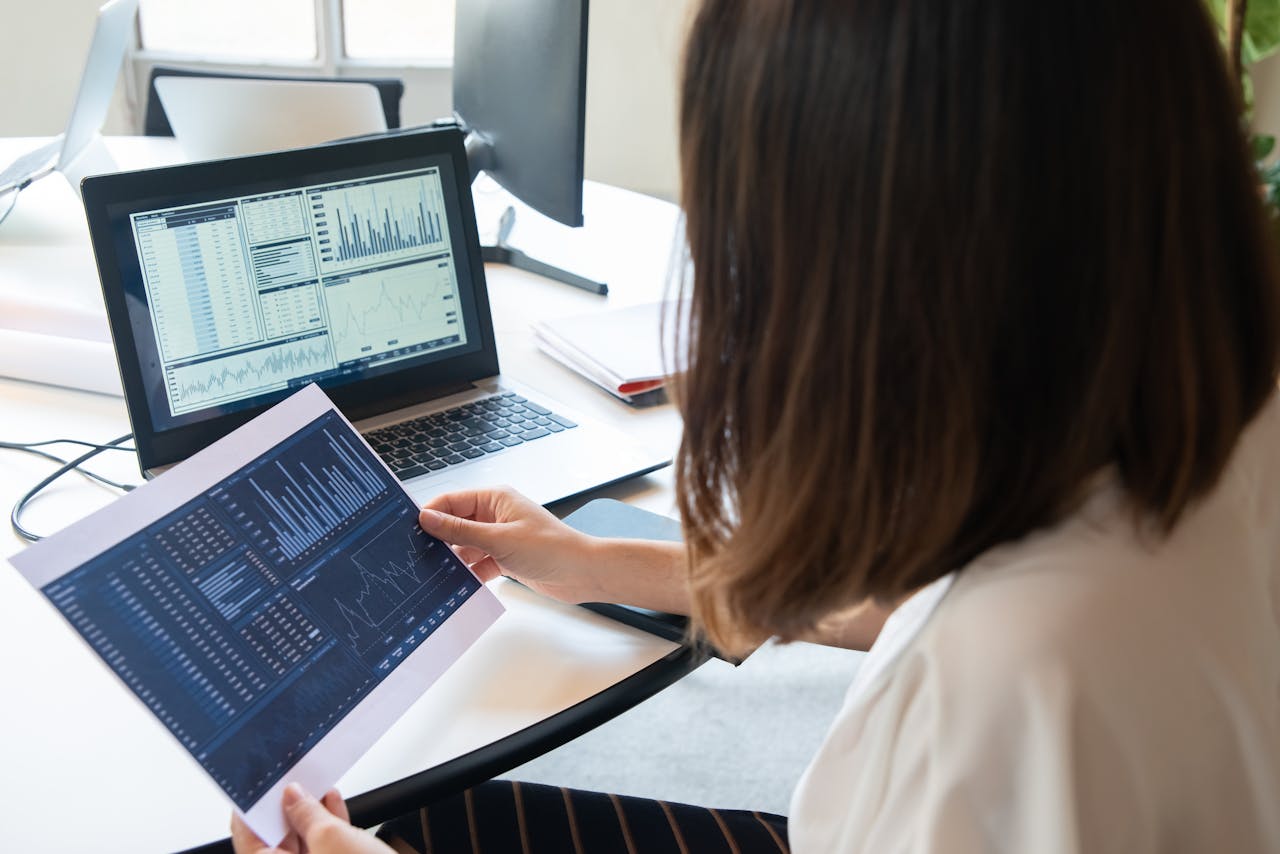 A professional woman analyzes financial charts on a laptop and paper for business insights.